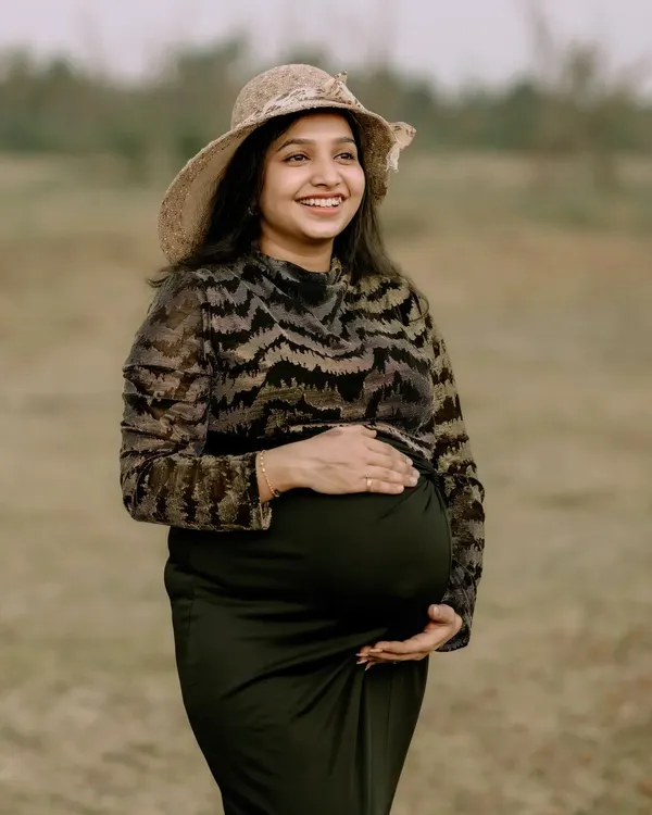 A solo maternity portrait capturing the pure happiness of a mother-to-be. Her joyful smile and the natural, open field setting create a sense of peace and contentment. The simple hat adds a touch of timeless style.
