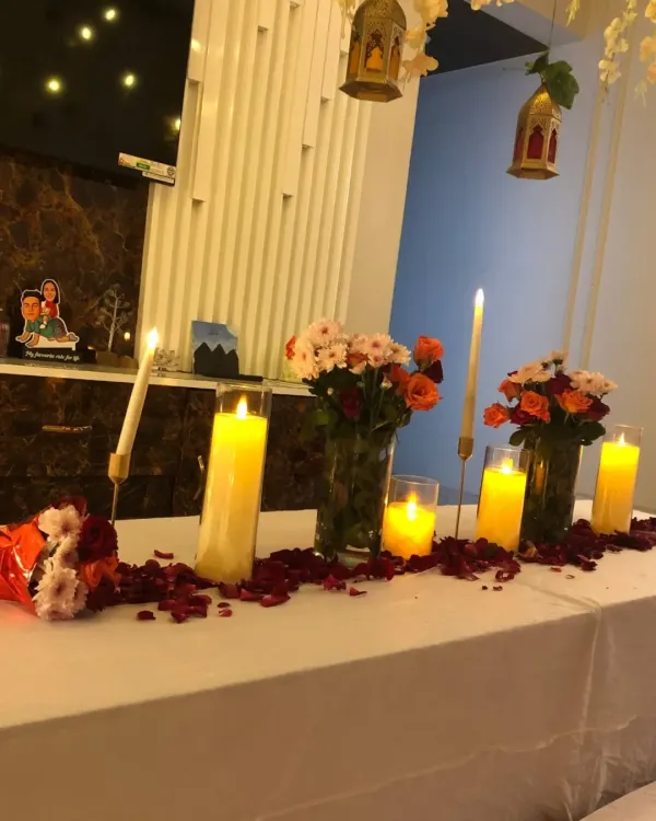 An intimate table setup for a romantic dinner, featuring multiple candles, fresh flower bouquets, and scattered rose petals.