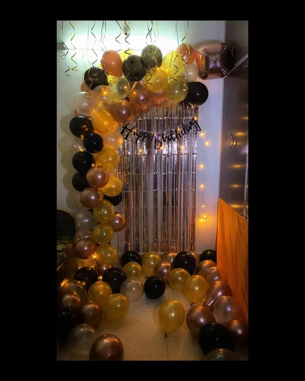 For this birthday surprise, I put together a stylish balloon arch using a mix of black, gold, and chrome balloons. The design is complemented by a shimmery silver curtain and warm fairy lights, creating a perfect backdrop for party photos.