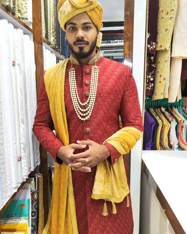 A classic red and gold combination for the groom. This textured red sherwani is paired with a gold turban and a velvet stole for a truly traditional and royal wedding look.
