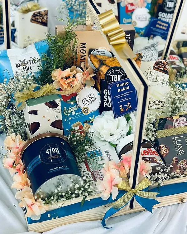 A beautifully arranged luxury snack hamper in a wooden basket, overflowing with premium products like 4700BC popcorn, Nutella, Smoor chocolates, and TBH snacks. This bespoke gift is perfect for festive occasions like Diwali or as a high-end corporate present.