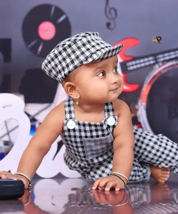 A little rockstar in the making! This baby in a checkered outfit and cap looks cool and confident in a music-themed setup, complete with guitars and records.
