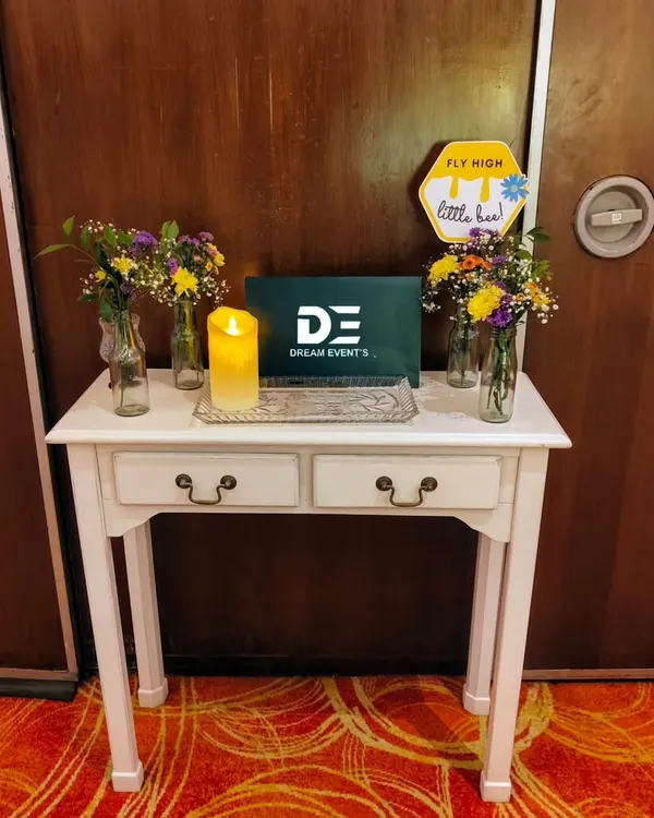 A charming welcome table setup for a first birthday party, featuring a small easel, fresh flower vases, and a candle to greet guests.