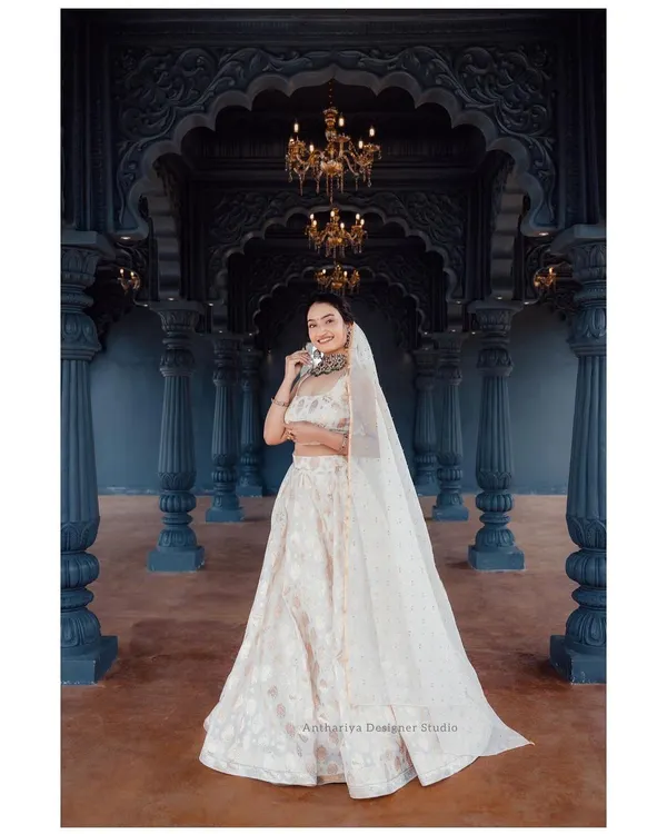 This full-length view shows the grandeur of our off-white brocade lehenga. Set against a regal backdrop, this outfit is a perfect rental choice for a bride's reception or a formal evening event.