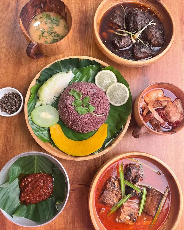 A complete Naga meal experience served with love. This plate features traditional purple rice with a beautiful smiley face arrangement, surrounded by Anishi smoked pork, pork with bamboo shoot, fiery King Chilli chutney, boiled vegetables, and a simple dal. This is how we share food at home, and it’s how I want you to feel when you eat with us.