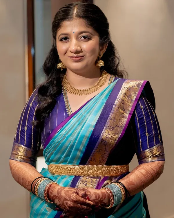 A full portrait of a client looking radiant in her silk saree. The mehendi on her hands and forearms adds a traditional and celebratory element to her elegant look.