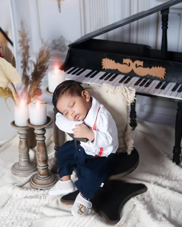 Dressed in a tiny shirt and suspenders, this baby boy dozes peacefully while leaning against the piano stool. It's a charming and creative pose that adds a story to the portrait.