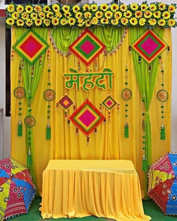A classic Mehendi ceremony backdrop with bright yellow and green drapes, colorful hangings, and traditional umbrellas.