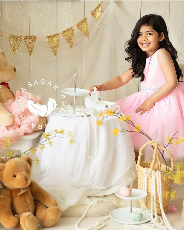 A whimsical toddler portrait session. This little girl is enjoying a make-believe tea party with her teddy bear, her bright smile showing how much fun she's having.