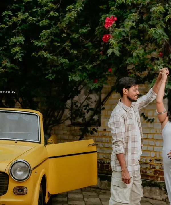 A playful shot of a couple dancing next to a bright yellow vintage car, adding a fun, retro vibe to their maternity photoshoot.