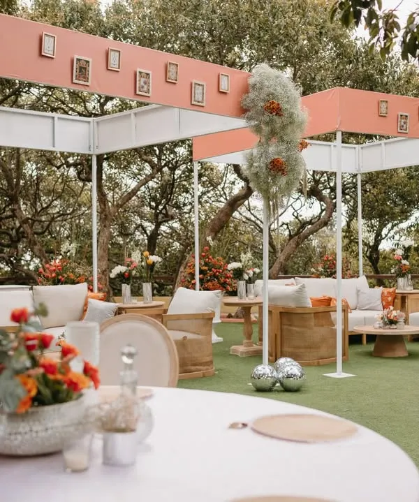 A modern and chic outdoor lounge setup for a daytime wedding ceremony, featuring clean lines, comfortable seating, and personalized photo frames on the canopy.