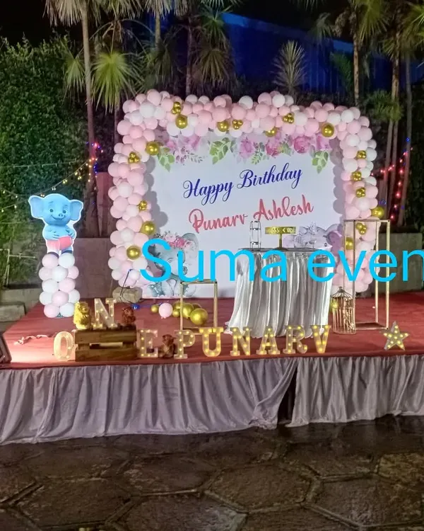 An elegant outdoor stage decoration for Punarv and Ashlesh's birthday. This setup features a large floral backdrop framed by a pink and white balloon arch, set on a professionally draped stage.