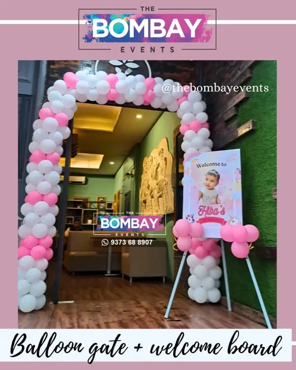 Make your child's birthday entrance magical. This setup for a first birthday features a pink and white balloon arch and a personalized welcome easel with the birthday girl's photo and a unicorn theme.