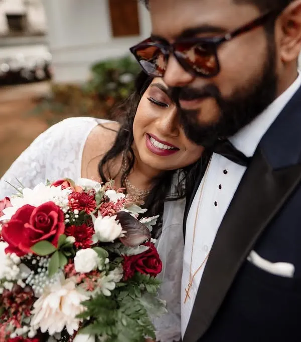 A tender moment between a bride and groom after their ceremony, with the bride holding a beautiful bouquet of red and white roses.