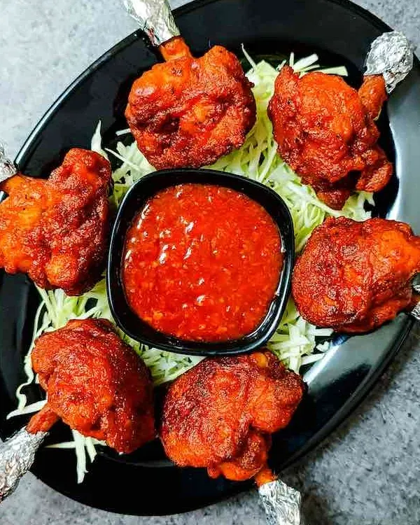 My Chicken Lollypops are crispy on the outside and juicy on the inside. They are served on a bed of shredded cabbage with a side of spicy red dipping sauce.