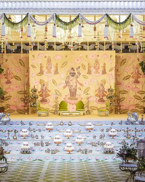 The 'Eternal Krishna' comes to life in this opulent mandap design. The backdrop features intricate Pichwai-style paintings, while the stage is lined with rows of traditional brass lamps, creating a regal and divine atmosphere for the wedding ceremony.