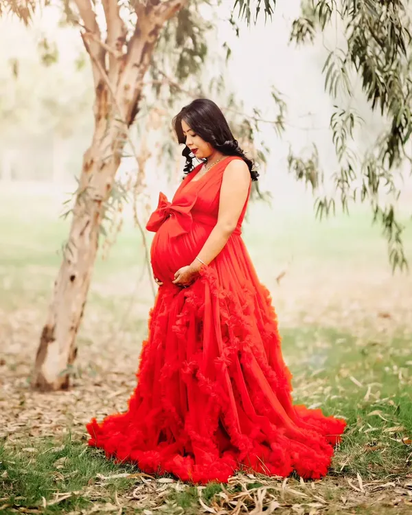 A beautiful outdoor maternity portrait taken in a lush, green park. The mom-to-be looks serene in a flowing red gown, creating a stunning contrast with the natural surroundings.