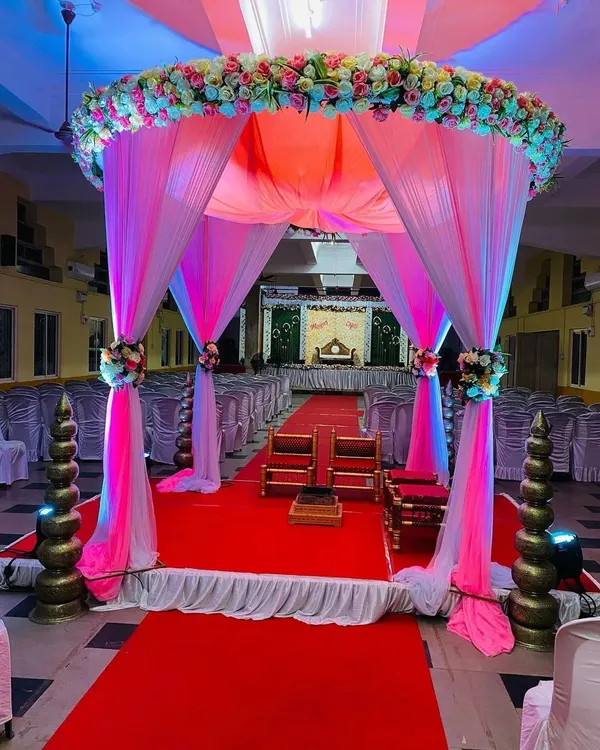 A breathtaking view down the aisle towards the wedding mandap. The entrance is framed by a canopy of pink and white drapes and flowers, creating a grand and romantic pathway for the ceremony.