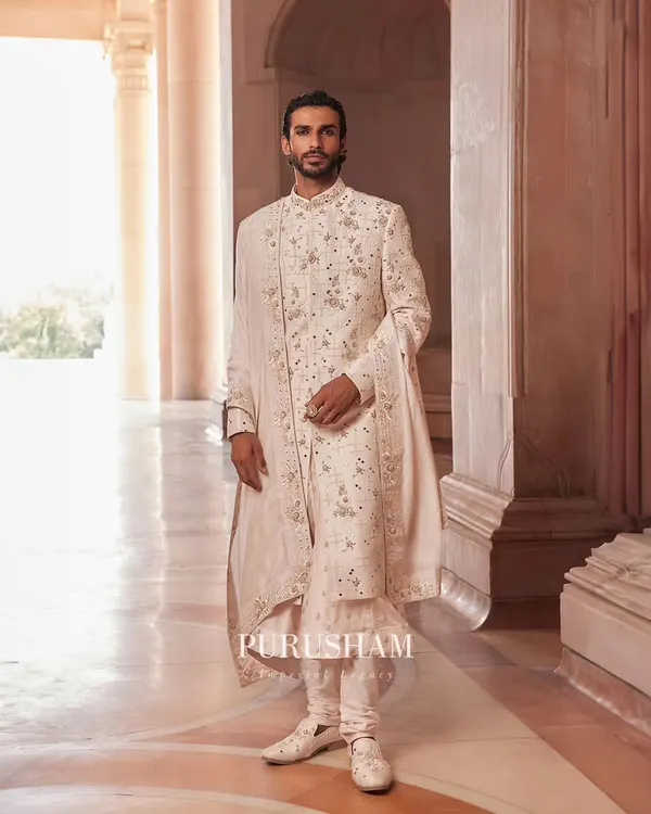 From my 'Takht' collection, this ivory sherwani is a study in grandeur. The surface is adorned with delicate, shimmering handwork, paired with a matching stole for a look of pure, understated royalty.