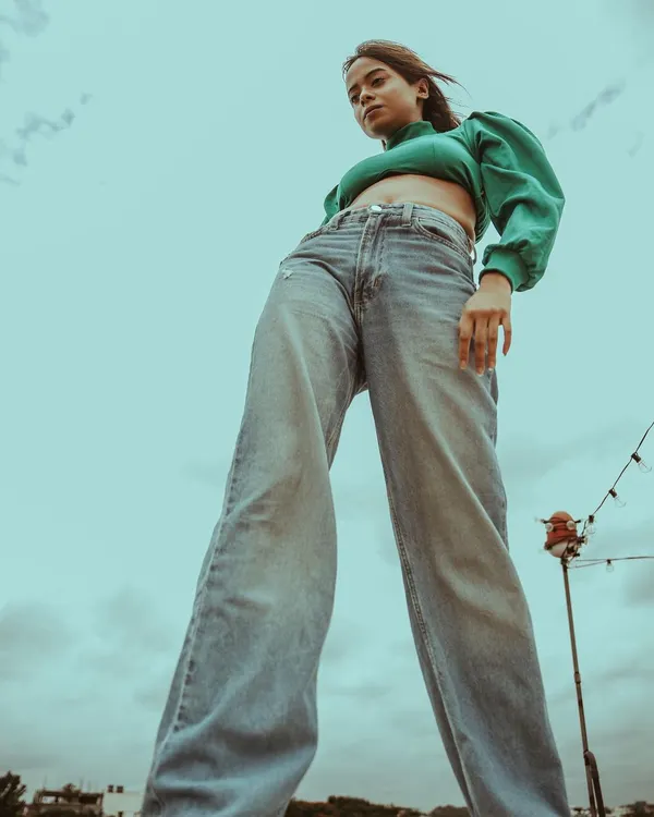 A low-angle shot that creates a powerful and confident look. The combination of a green puff-sleeve top and wide-leg jeans against the open sky gives this portrait a bold, modern edge.