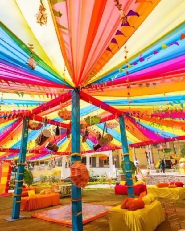 This vibrant, multi-colored canopy is my signature style for creating a festive and energetic atmosphere, perfect for a daytime Mehendi or Haldi event. I use long swathes of fabric to build a rainbow ceiling that instantly makes the space feel grand and joyful.