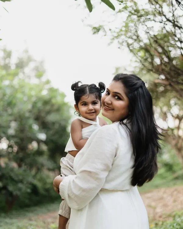 A mother holds her toddler daughter in a lush green garden. The natural light and beautiful surroundings create a soft and lovely portrait.