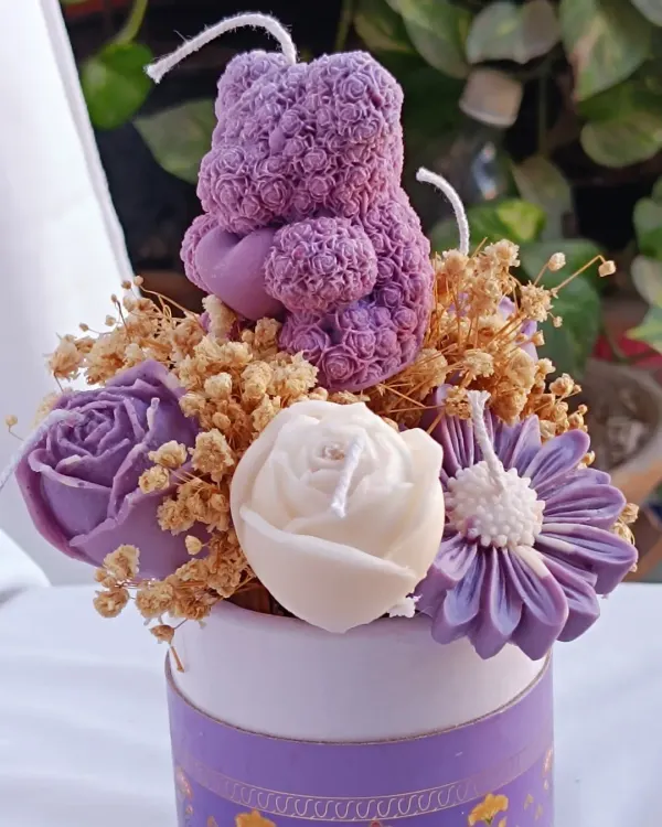 This is a beautiful flower bouquet candle arrangement in a decorative purple box. It features a purple teddy bear candle, roses, and daisies, accented with dried baby's breath.