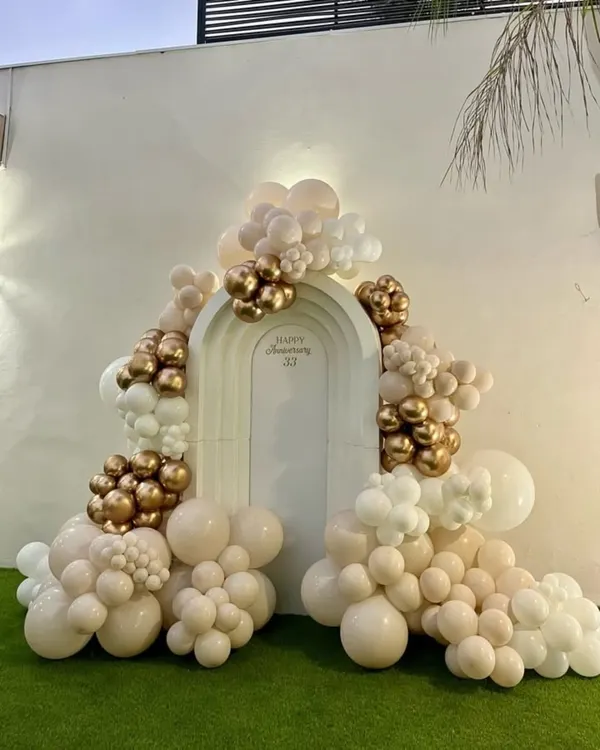 Elegance for a milestone celebration. This custom anniversary backdrop features a sophisticated organic balloon garland in nude, white, and chrome gold tones, creating a perfect photo opportunity for the happy couple.