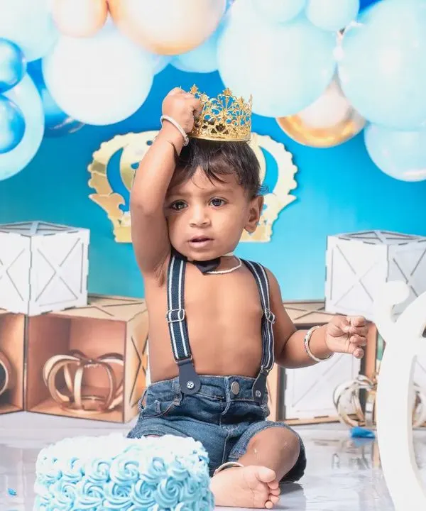 A little prince celebrating his first birthday with a royal blue cake smash. The setup includes a crown, balloons, and a delicious-looking cake ready to be smashed.