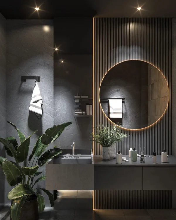 A luxurious dark-themed bathroom design. This space uses slate-grey tiles, a backlit circular mirror, and ribbed wall paneling to create a moody and sophisticated atmosphere, enhanced by indoor plants.