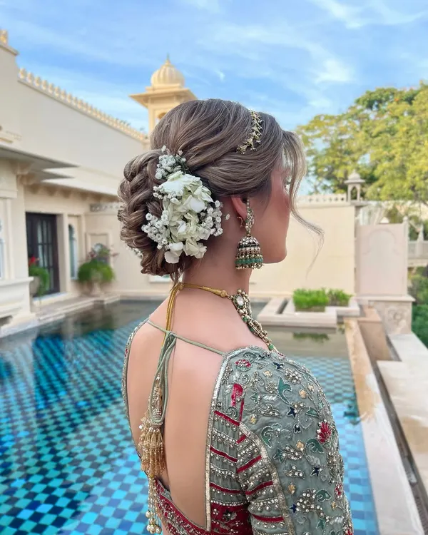 This intricate floral updo is one of my signature styles, perfect for a wedding day. The combination of a textured, woven bun with fresh white flowers creates a look that is both timeless and romantic, set against a stunning poolside backdrop in Udaipur.