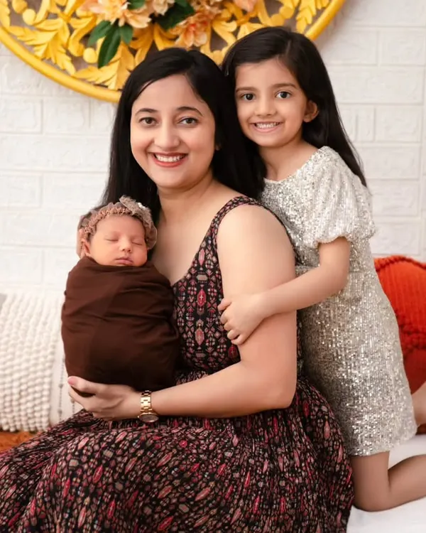 A mother sits with her older daughter, who lovingly embraces her and the new baby. This portrait highlights the joy of a growing family, capturing the special bond between a mother, her first child, and the newest arrival.