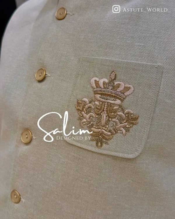 A close-up of the hand-embroidered crown crest on a beige Jodhpuri jacket. This kind of custom detail adds a regal and personal touch to your outfit.