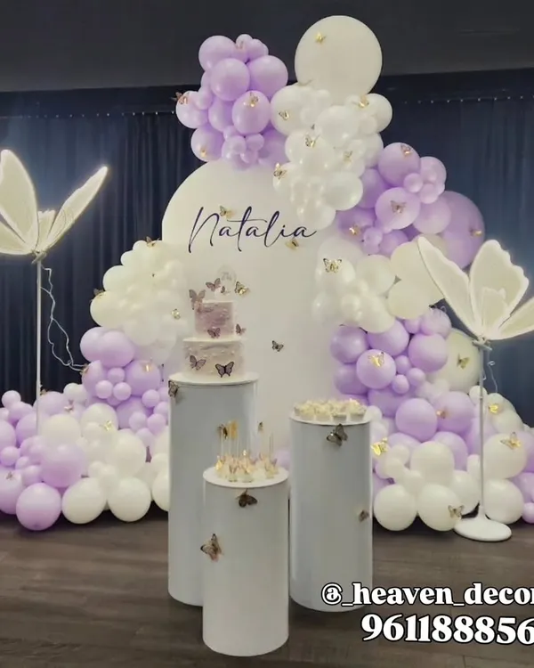 An elegant and ethereal butterfly theme in lavender and white, perfect for any age. The setup features an organic balloon cloud, large illuminated butterfly props, and minimalist white plinths for a sophisticated look.