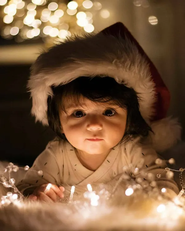 A close-up portrait of a newborn celebrating their first Christmas. We used soft fairy lights and a festive Santa hat to create this warm, magical moment, highlighting the baby's innocent expression.