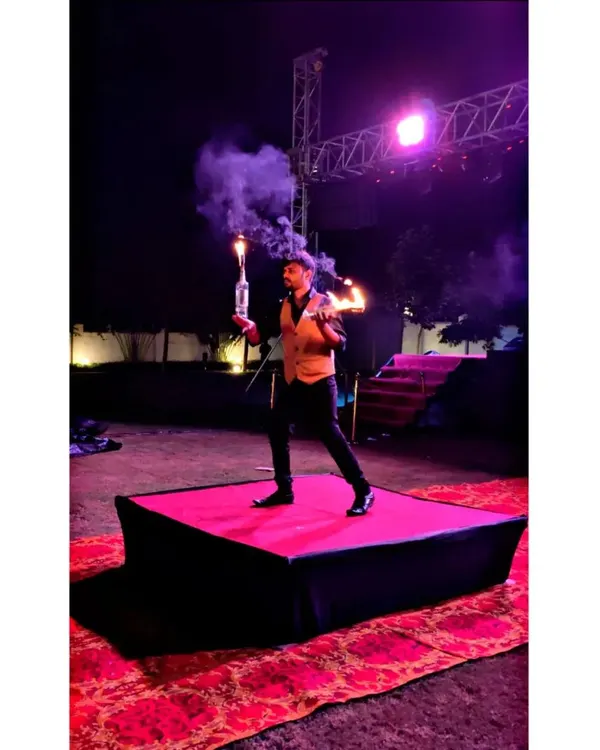 A bartender captivates the audience with a fire flair performance on a dedicated stage. The combination of fire, smoke, and skilled juggling adds a theatrical element to any outdoor event or sangeet night.
