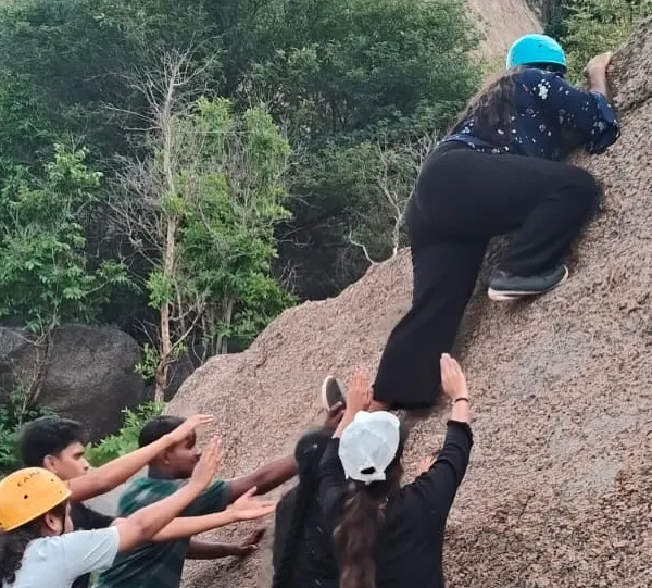 Teamwork is crucial in bouldering. Here, a group of students spots a climber, ensuring her safety as she navigates a rock face in Ramanagara.