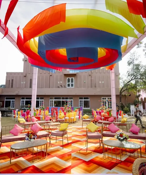 A vibrant, colorful Mayra setup in Agra. The overhead canopy of multi-colored drapes and eclectic seating creates a festive and playful atmosphere for a daytime event.
