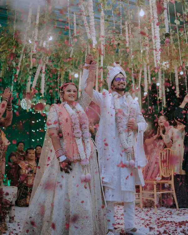 A moment of pure triumph and joy. As flower petals rain down, the newly married couple raises their hands in celebration, surrounded by the love of their family and friends.