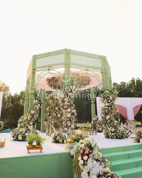 A full view of the French garden-inspired mandap, with its soft green lattice structure and abundant pastel florals creating a romantic focal point on the lush lawn.