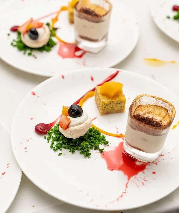 An exquisite plated dessert I created for a 50th birthday celebration. It features a trio of treats: a mini tiramisu, a delicate meringue with fruit, and a small cake, all artfully arranged.