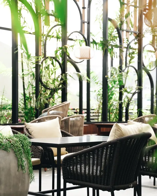 A close-up on the details. The interplay of textures, from the woven chairs to the lush greenery, creates a rich visual narrative about the cafe's design aesthetic.