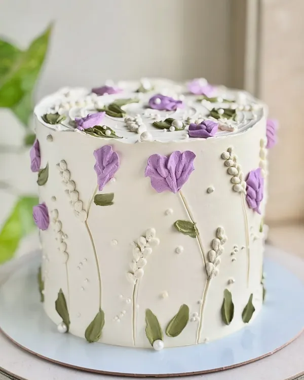 A little garden in bloom, but make it cake. This design features hand-piped lavender and white wildflowers, creating a delicate and artistic floral pattern around the entire cake.