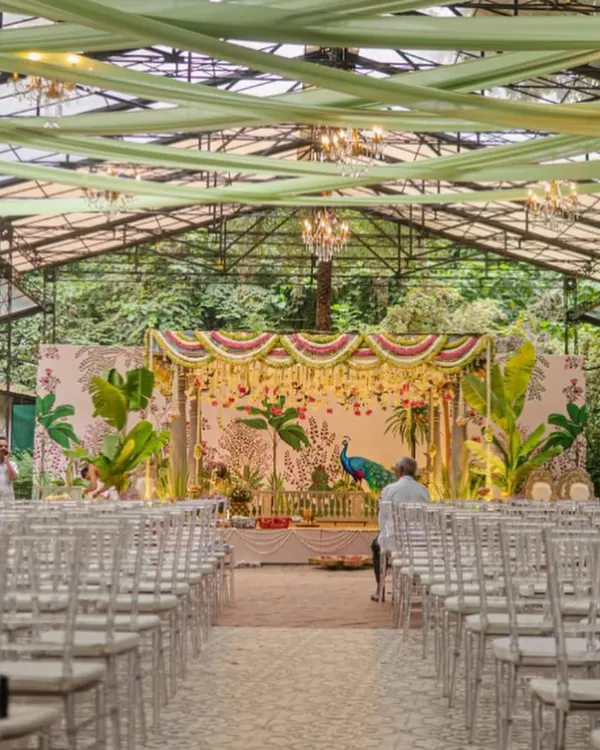 We designed this stunning South Indian wedding mandap in a glasshouse, blending the lush green outdoors with traditional decor. The custom-painted backdrop featuring a majestic peacock and tropical foliage created a vibrant yet sacred atmosphere for the ceremony.