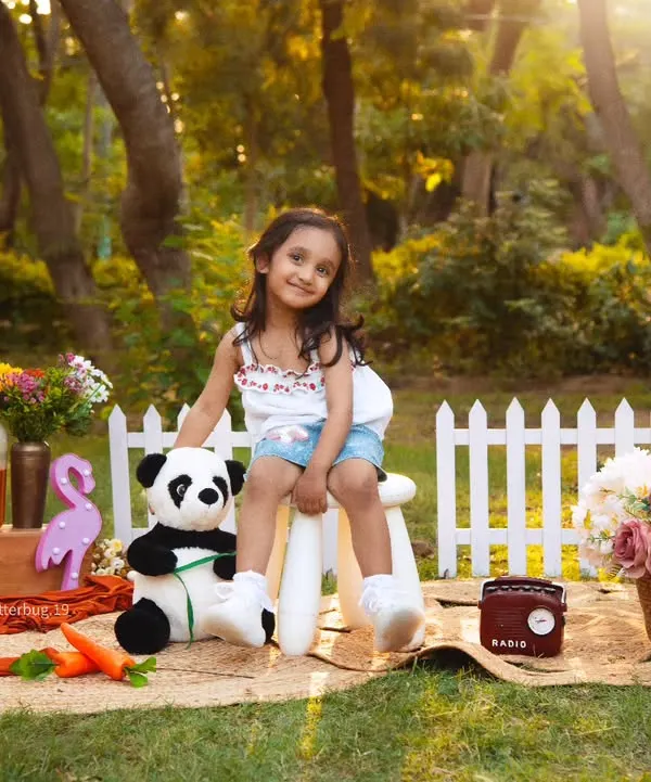 A lovely outdoor portrait of a four-year-old girl enjoying a picnic in the park, surrounded by flowers and sunshine.