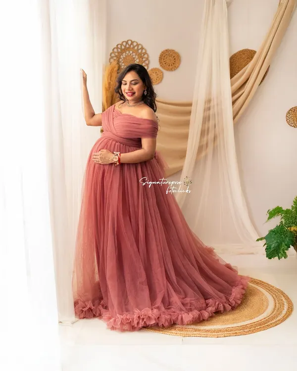 A beautiful solo portrait in a mauve gown, with the mother-to-be looking out a window, bathed in soft, natural light.