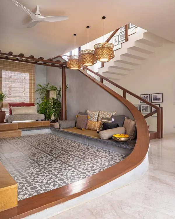 This living area features a modern take on the traditional 'thinnai' or raised verandah seating. The curved, built-in bench is paired with patterned floor tiles and woven pendant lights for a look that is both contemporary and classic.