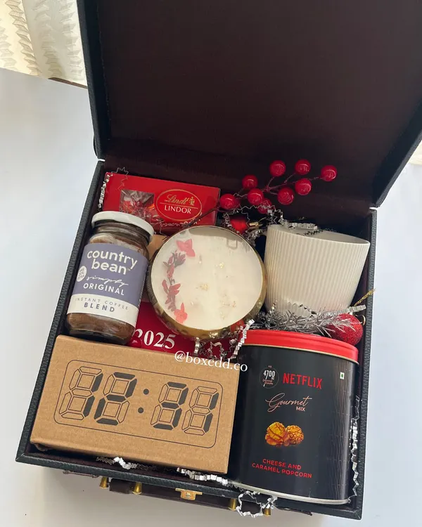 A luxurious New Year gift packed in a leatherette trunk. It includes an LED clock, a 2025 calendar, gourmet popcorn, coffee, and a scented candle to welcome the new year.
