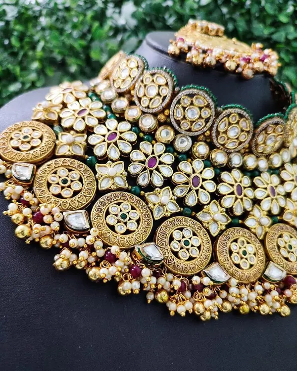 A close-up of a very grand and intricate bridal choker available for rent. This piece features multiple layers of kundan, filigree work, and colored stones, designed to make a statement.