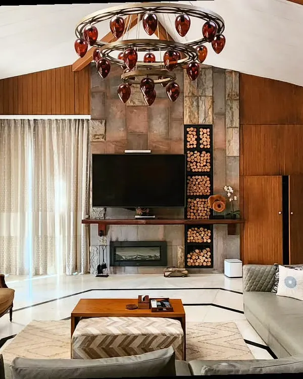 We brought warmth and character into this Dehradun Haveli by pairing natural stone and rich wood. This living room renovation features a striking stone fireplace, custom wood paneling, and a unique chandelier, creating a space that is both grand and inviting.